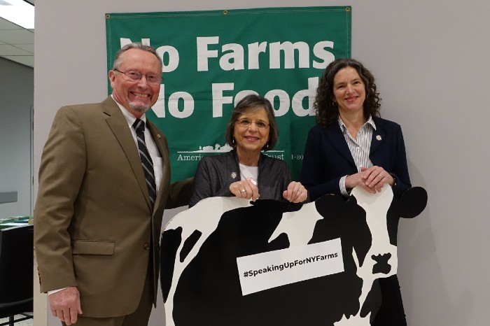 State leaders pose with wooden cow and No Farms No Food banner at New York State Capitol.