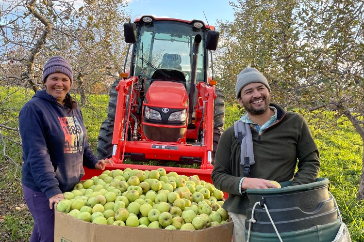 Carlos and Lorena stand with a bin of apples