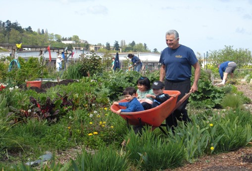 A man pushes a young child in a wheelbarrow in an urban garden in Seattle, Washington